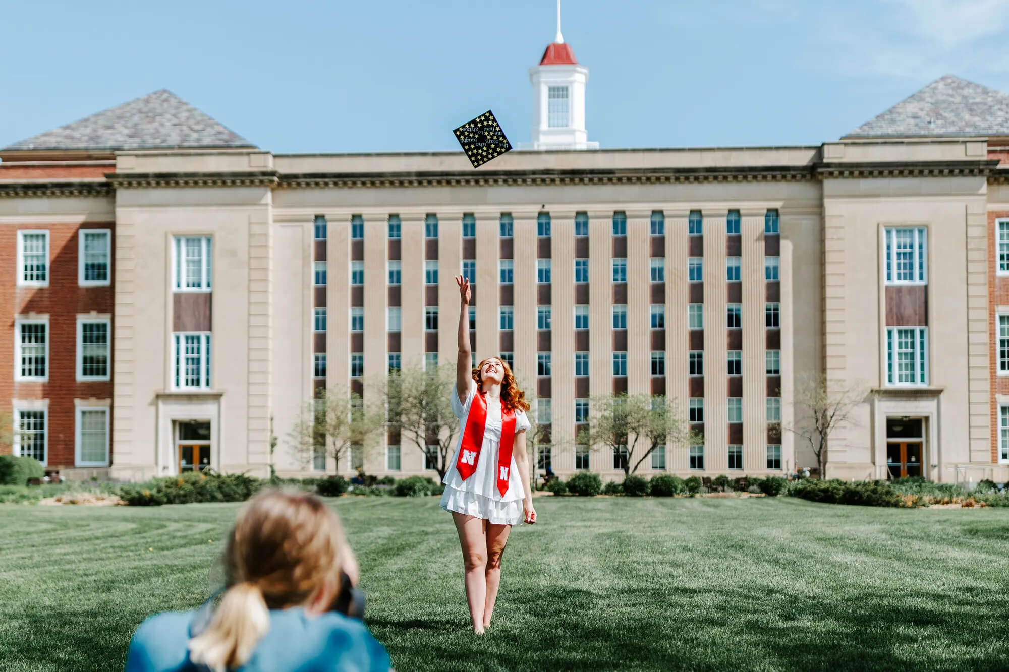 Graduate tossing cap in front of Love Library, with photographer in the foreground.