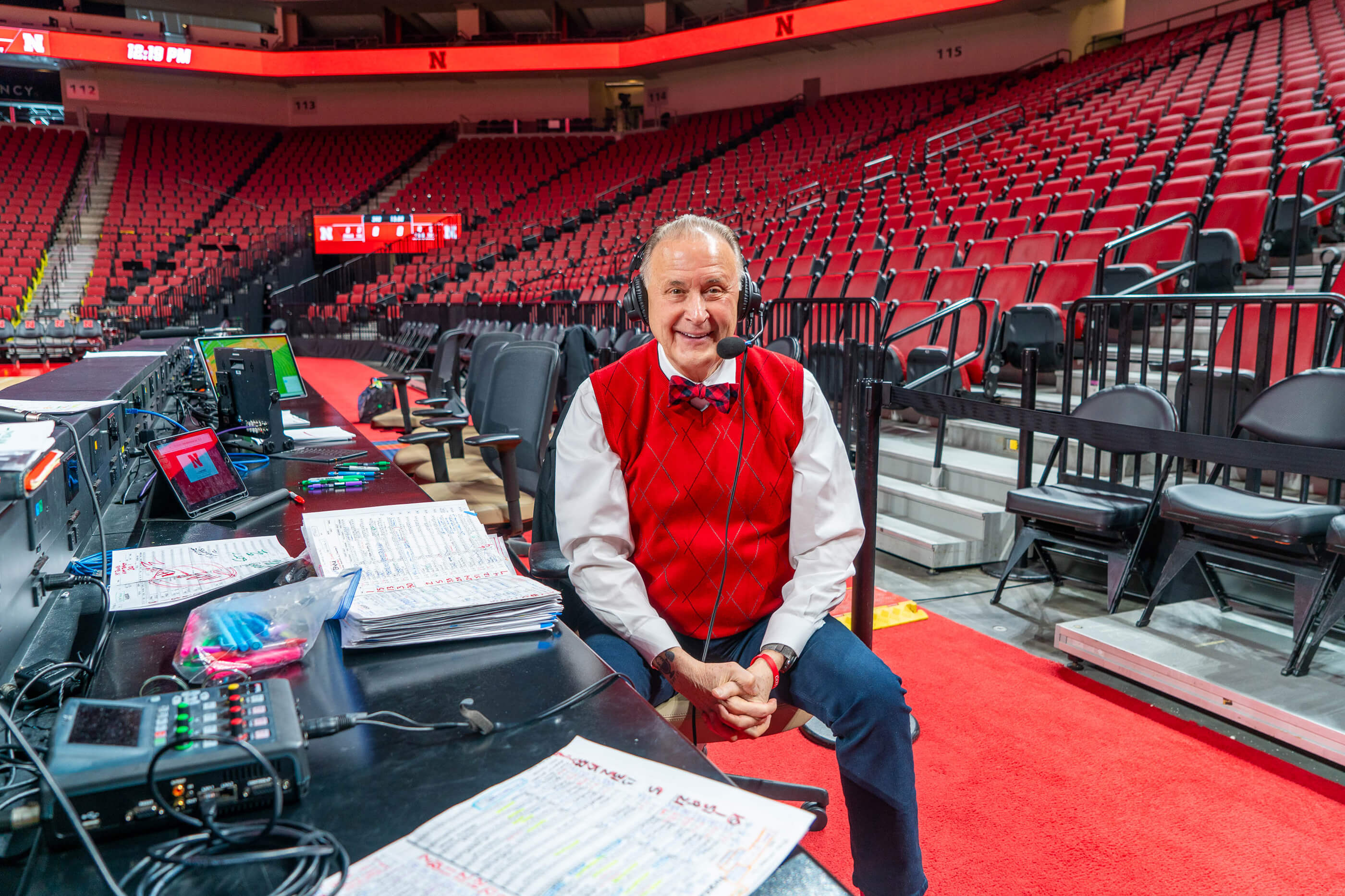 Radio announcer sitting in chair in front of equipment on sideline in Pinnacle Bank Arena