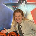 Shelby Jacobs smiles and stretches out her arms in front of backdrop with basketball logo and orange Wilson basketballs in the foreground.