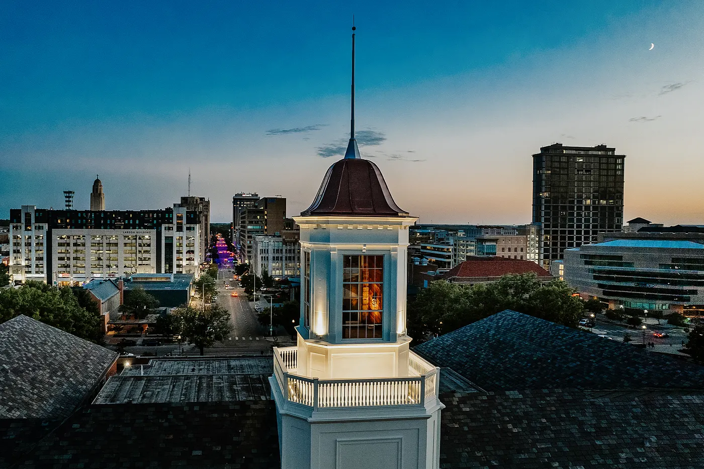 The sun sets on Lincoln with the Love Library cupola in the foreground and downtown Lincoln in the distance