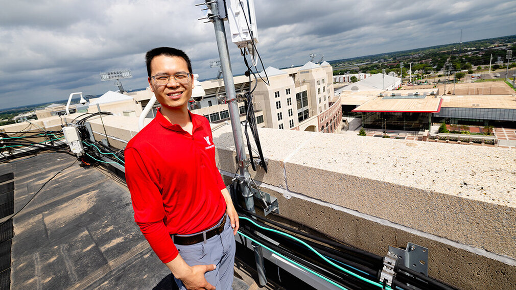 Qiang Liu, assistant professor in the School of Computing, stands next to one of the Husker-Net 5G amplifiers topping the roof of Oldfather Hall. Husker-Net is the University of Nebraska–Lincoln&#039;s private 5G network, and one of Liu&#039;s research focuses.