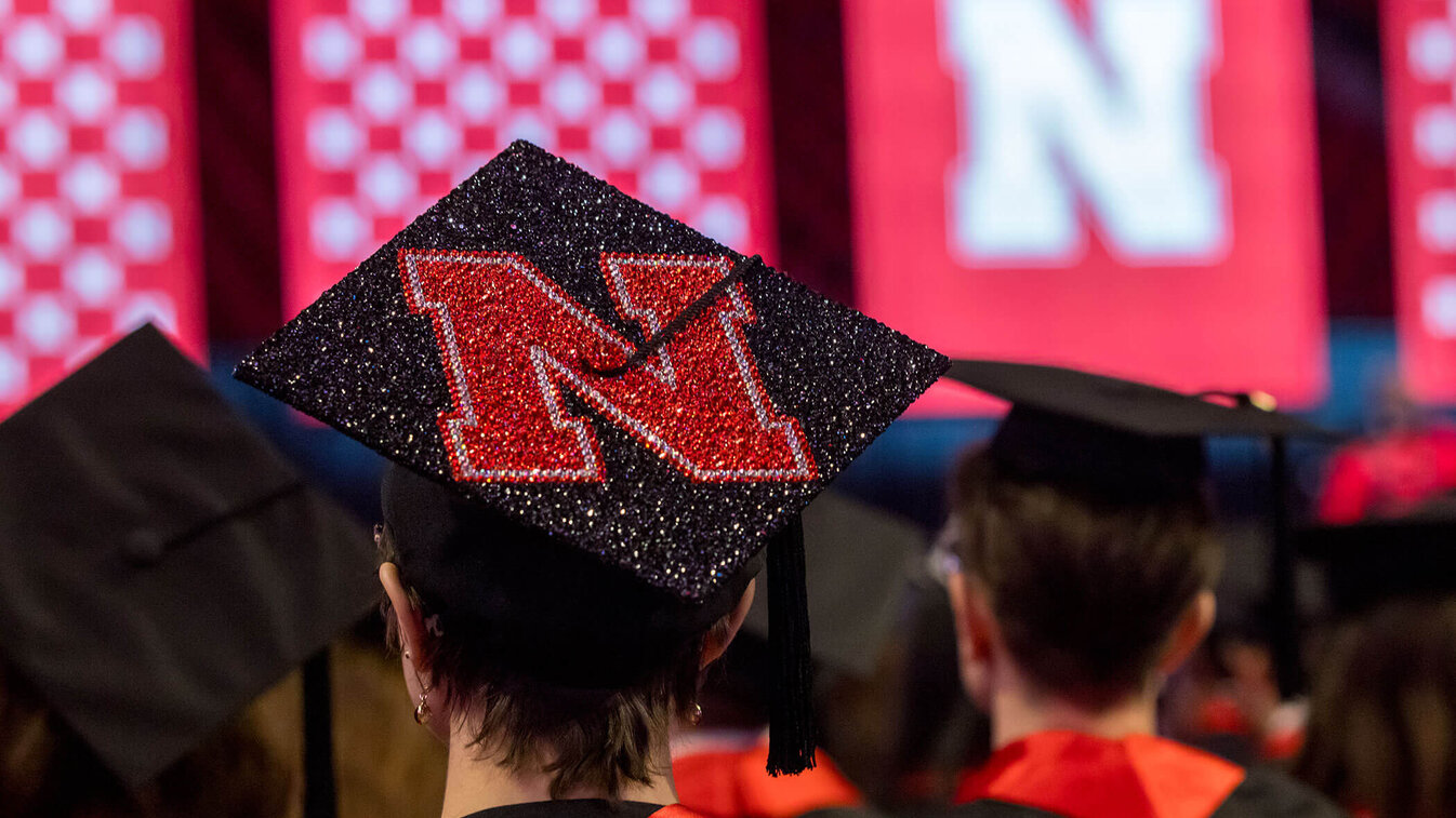 Graduation cap with a red glittery "N" in an auditorium with bright red banners.