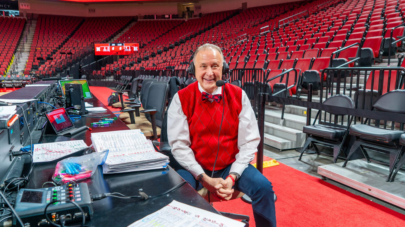 Radio announcer sitting in chair in front of equipment on sideline in Pinnacle Bank Arena
