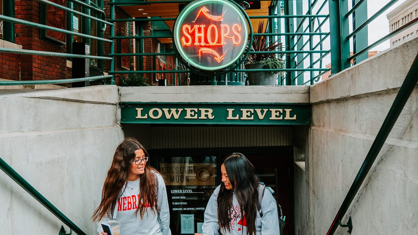 Students walk out of Crescent Moon under a neon sign that says “Shops”