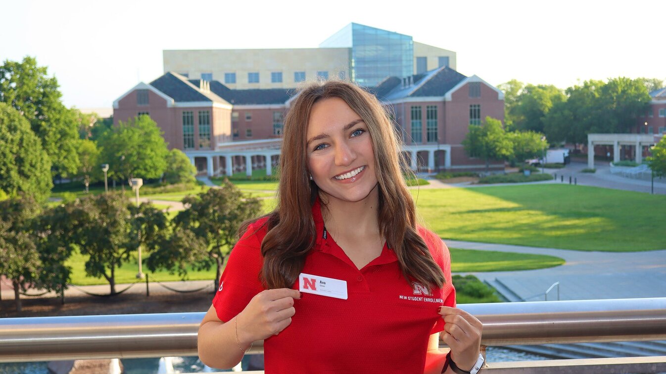Ava smiles for a photo in her NSE polo with campus in the background