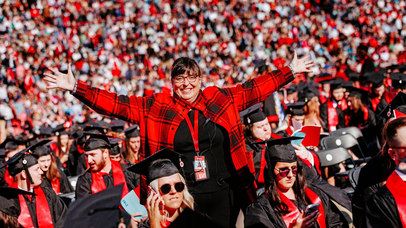 Annette smiles for a photo with her arms outstretched in a sea of Husker grads