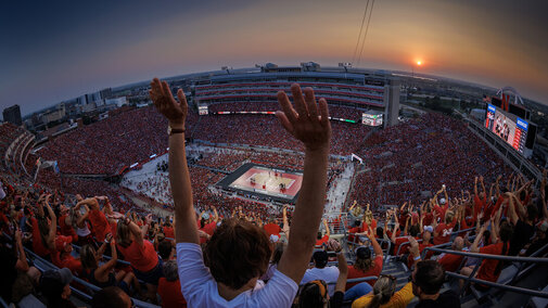 Fans raising arms while looking down at Volleyball court in Memorial Stadium