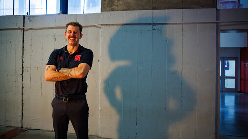 Connor smile for a photo in Memorial Stadium. On the wall behind him is the silhouette of Herbie Husker with his hands on his hips
