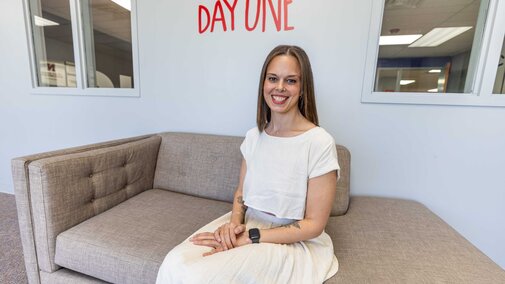 Woman seated on a gray couch in a bright office space, with a motivational phrase on the wall.