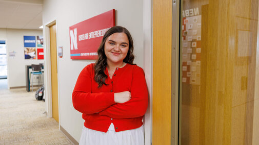 Student in red sweater and white skirt standing outside door of Center for Entrepreneurship