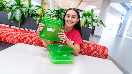 Student holding green recycled plastic storage containers