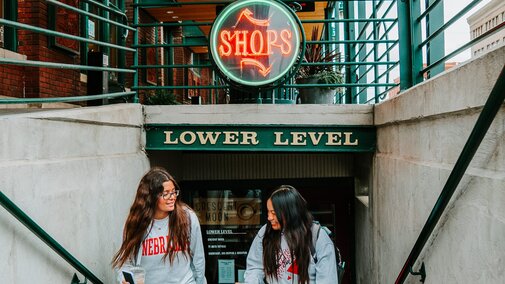 Students walk out of Crescent Moon under a neon sign that says “Shops”