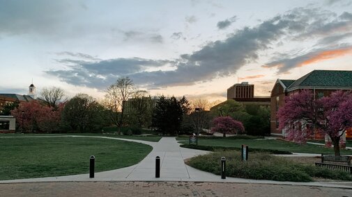 The sun sets on campus, shining on the top of Love Library in the distance