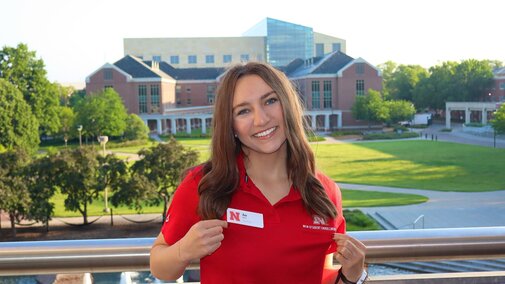 Ava smiles for a photo in her NSE polo with campus in the background