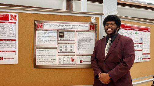 Marcus smiles for a photo next to his research poster titled: A survey of over-the-counter substance stability in animal tissues