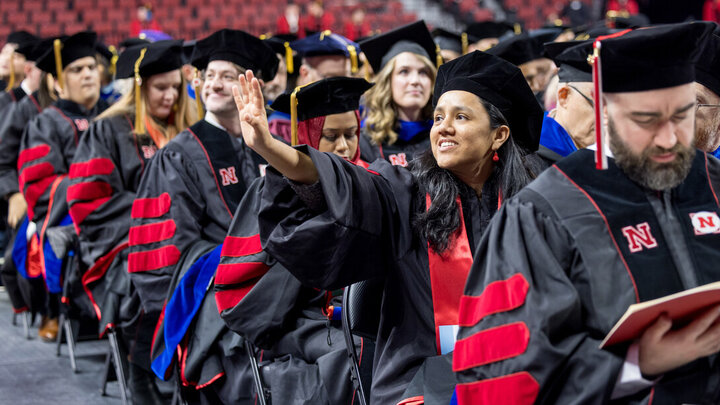 Heydi Calderon Ambelis Han, seated among fellow graduates, waves to family members in the crowd during the graduate and professional degree ceremony Dec. 19 at Pinnacle Bank Arena. She earned a doctoral degree in biological engineering.