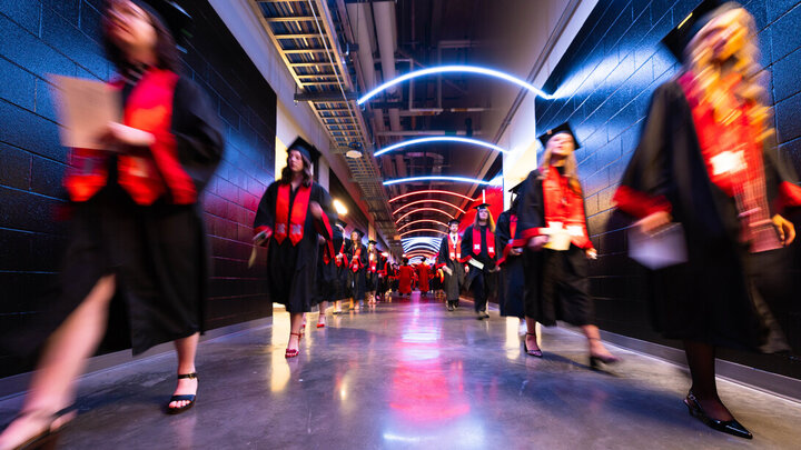 Two lines of graduates walk through a hallway in Pinnacle Bank Arena.