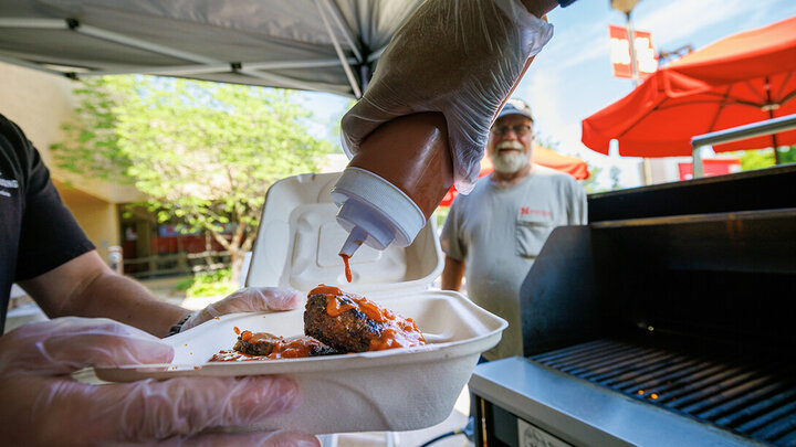 A cook adds Oklahoma BBQ sauce to an order of ribs at an East Campus grill out.