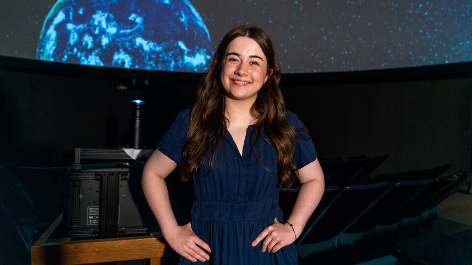 Student standing in front of projection of earth
