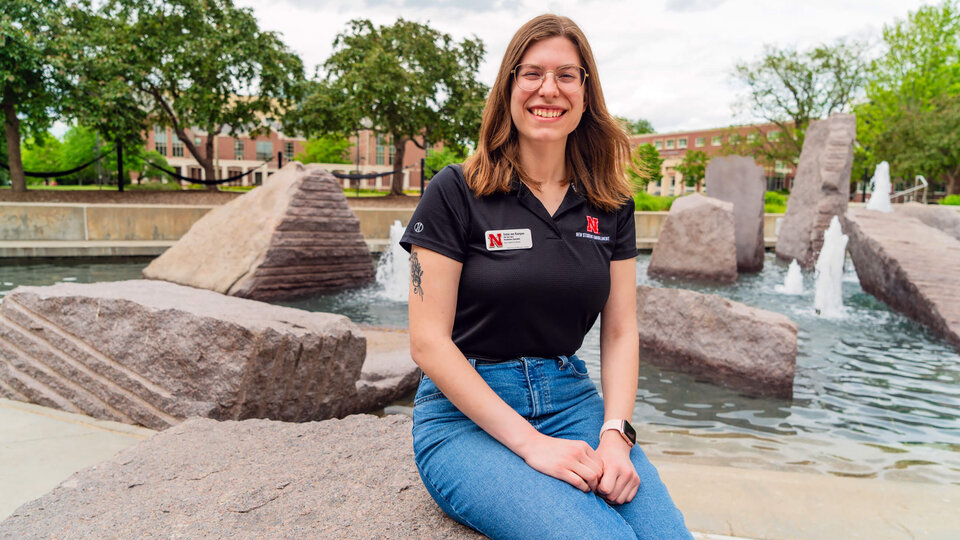 Student in black shirt wearing nametag sitting in front of fountain