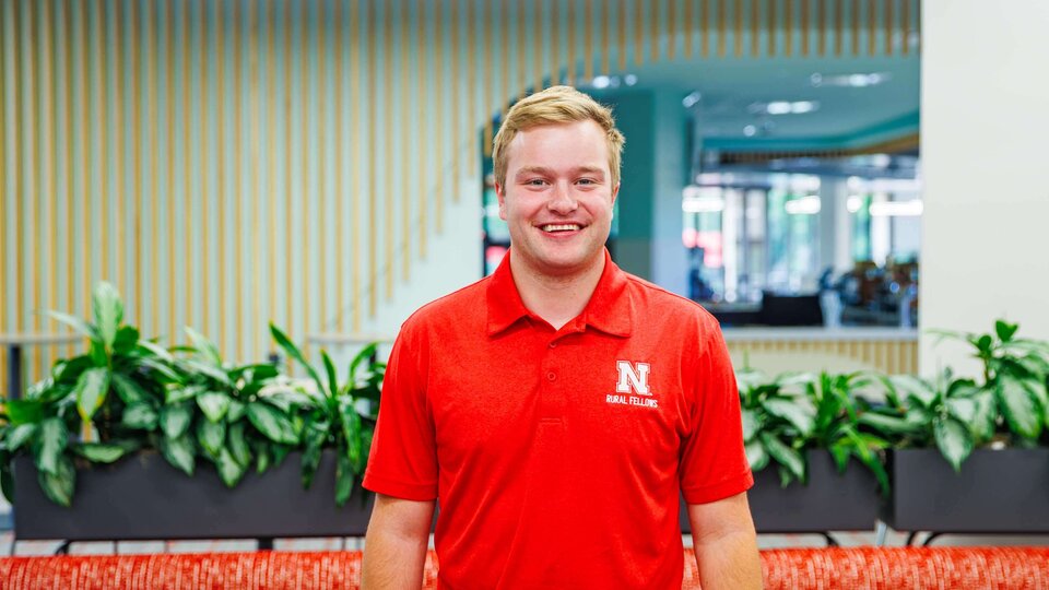 Man in a red polo shirt stands smiling in a building with plants and striped wall accents.