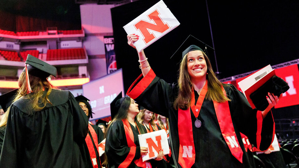 Graduate holding degree in air and smiling at Commencement ceremony in Pinnacle Bank Arena