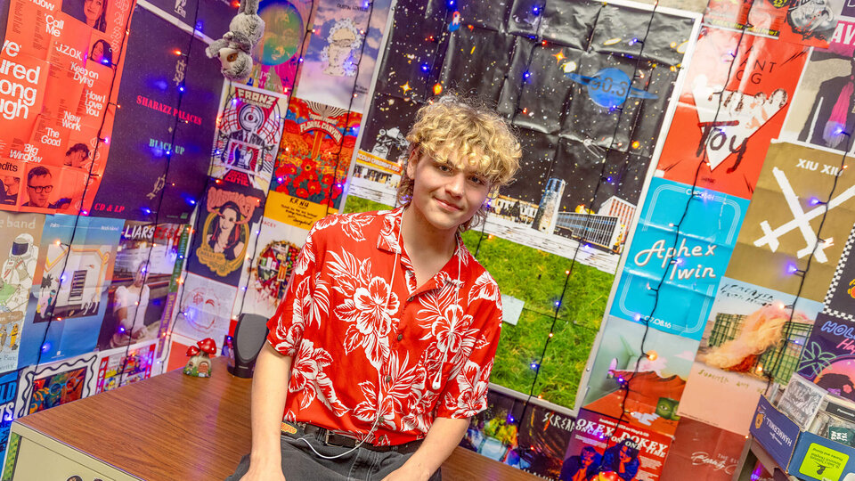 Student in red shirt sitting in room with walls covered by music posters