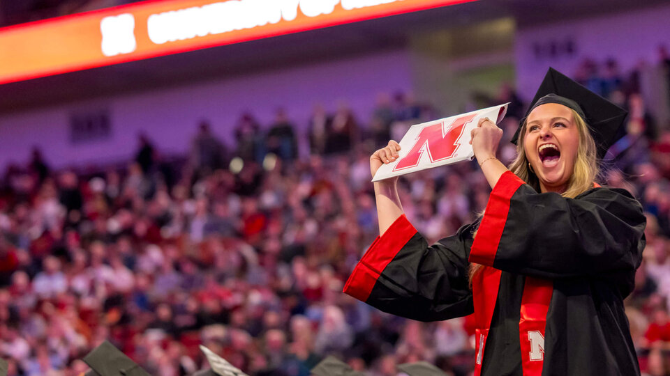 Graduate cheers and holds up diploma during December 2025 commencement ceremony at Pinnacle Bank Arena