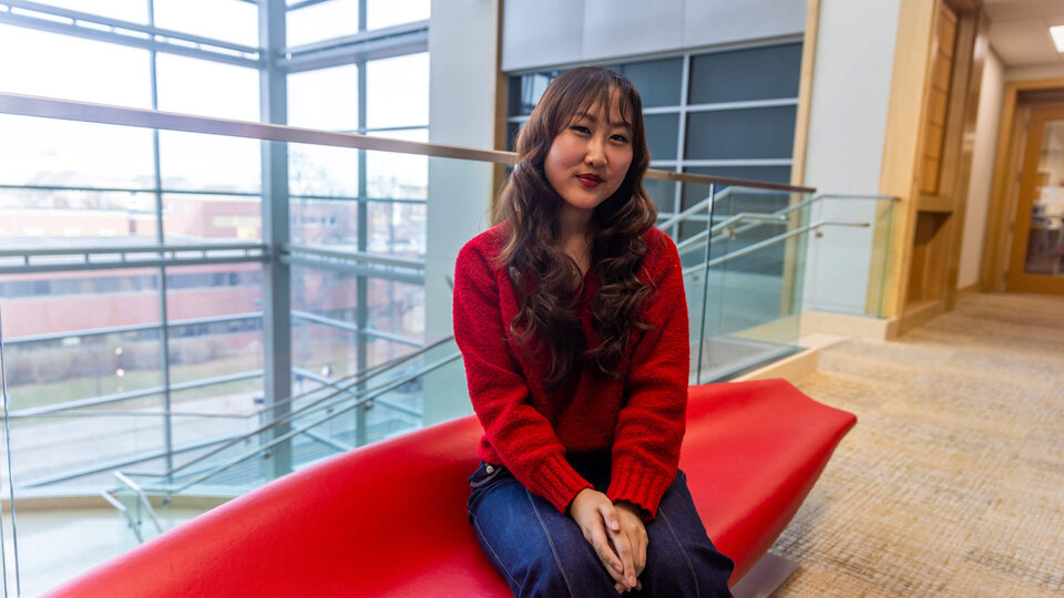 Student sitting on red modern bench in lobby of College of Business building