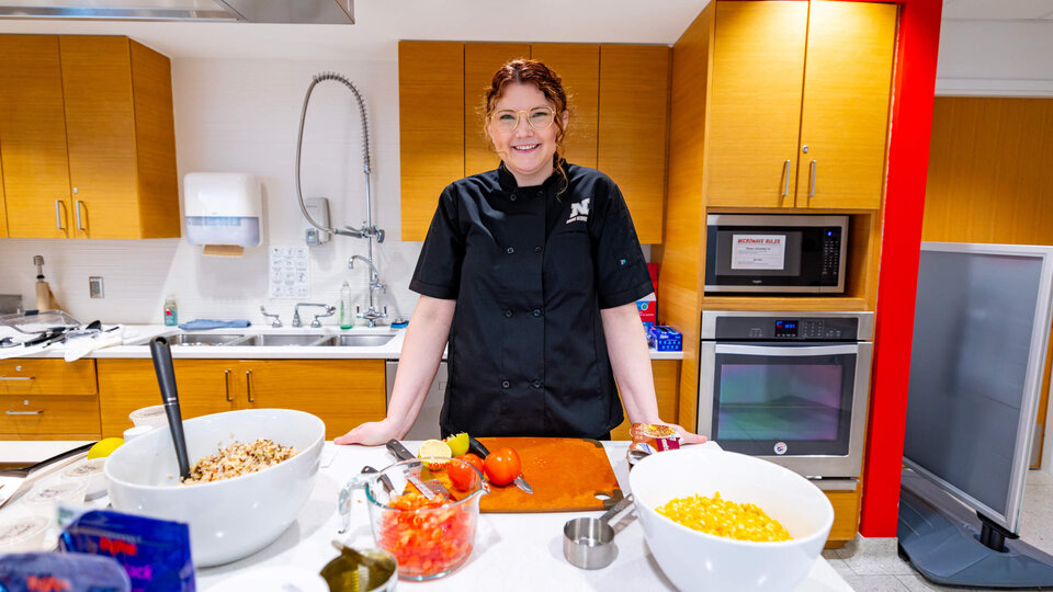 Chef in a modern kitchen with colorful ingredients and utensils on a counter.