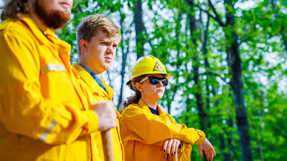 Students in yellow jackets watch field conservation instructor in forest