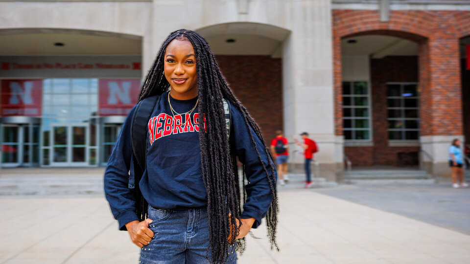 Smiling woman wearing a "Nebraska" sweatshirt stands outdoors in front of a campus building.