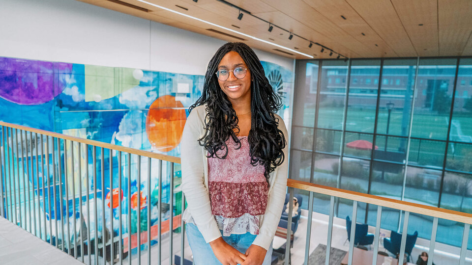 Student standing by railing inside atrium with large colorful painting on wall behind them