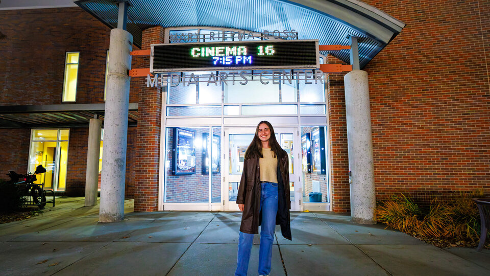 Student standing outside Mary Riepma Ross Media Arts Center with lit marquee