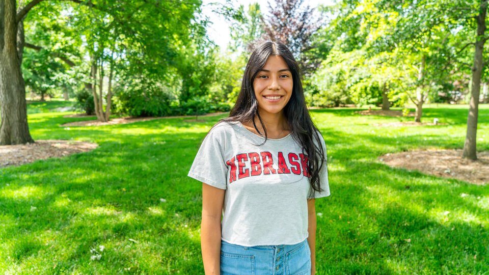 Student standing in grove of trees wearing Nebraska t-shirt