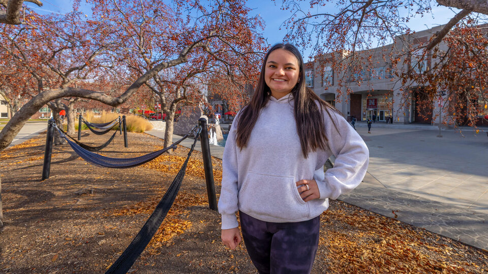 Student in gray sweatshirt standing by hammocks behind Nebraska Union