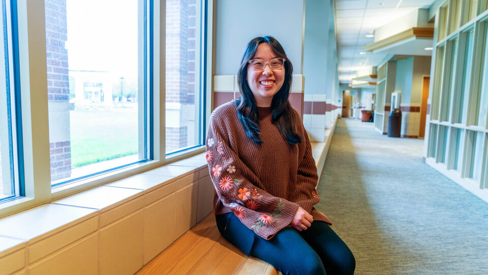 Student sitting on bench in front of window in Raikes School