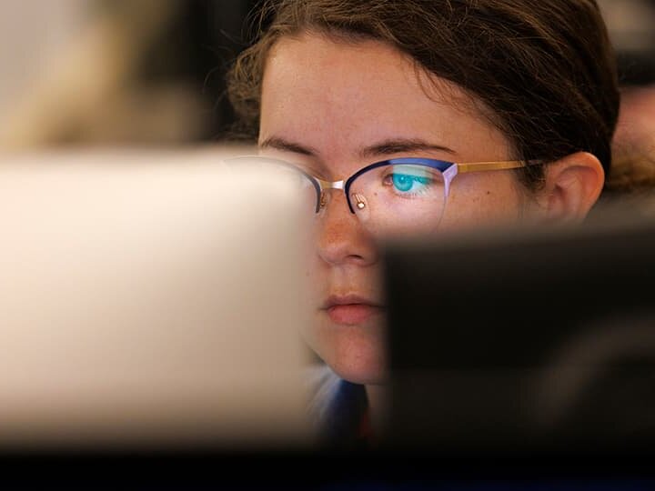 The eyes of a student appear behind a computer monitor, reflection from glowing screen in student's glasses