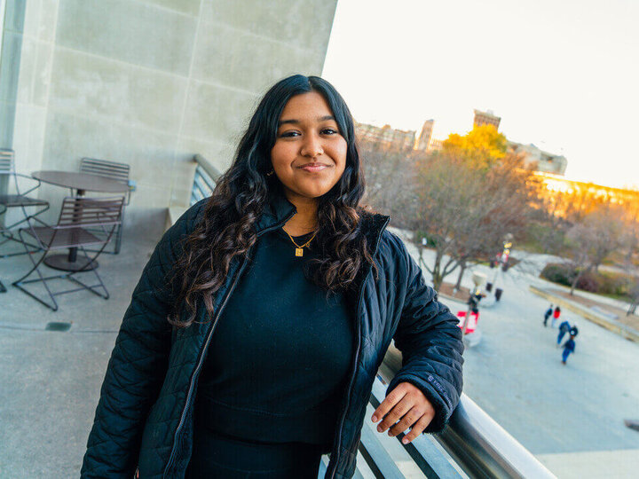 Student leaning on railing outside student union looking over greenspace