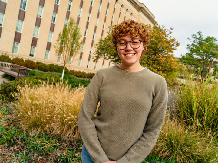 Student standing outside on green space in front of building