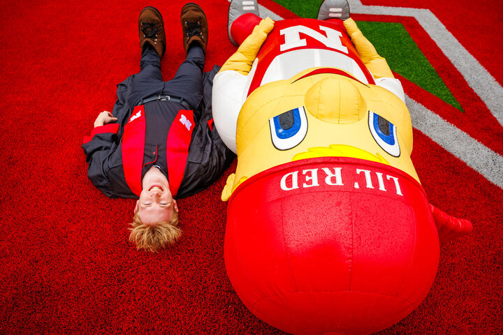 Aidan, wearing grad regalia, lays on the stadium turf beside Lil Red
