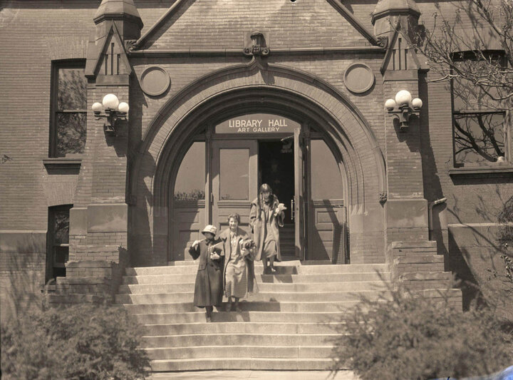 An archived photograph of three students walking out of the University Library, now Architecture Hall.