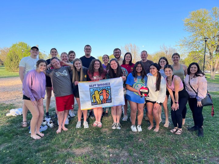 Jenny Castor and other members of the Best Buddies program get together for a group photo outside holding a banner at the center reading "Best Buddies."