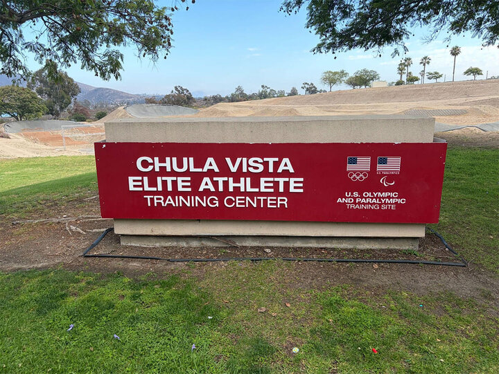 Red sign reads "Chula Vista Elite Athlete Training Center" amidst grassy landscape and distant hills.