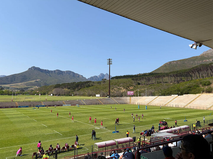 Players on a rugby field surrounded by mountains under a clear blue sky in South Africa..