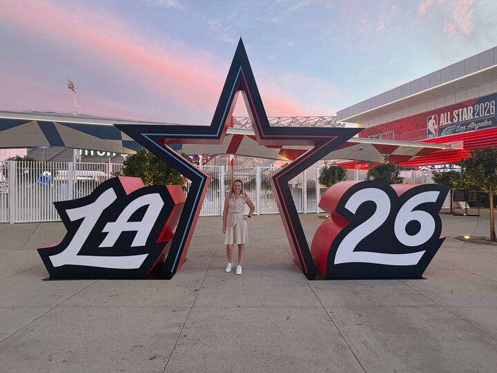 Large star structure with "LA" and "26" displayed, Shelby Jacobs stands within, sunset sky and event signage. Shelby served as the Chair of the NBA All-Star Planning Committee for NBA All-Star 2026 hosted at Intuit Dome.