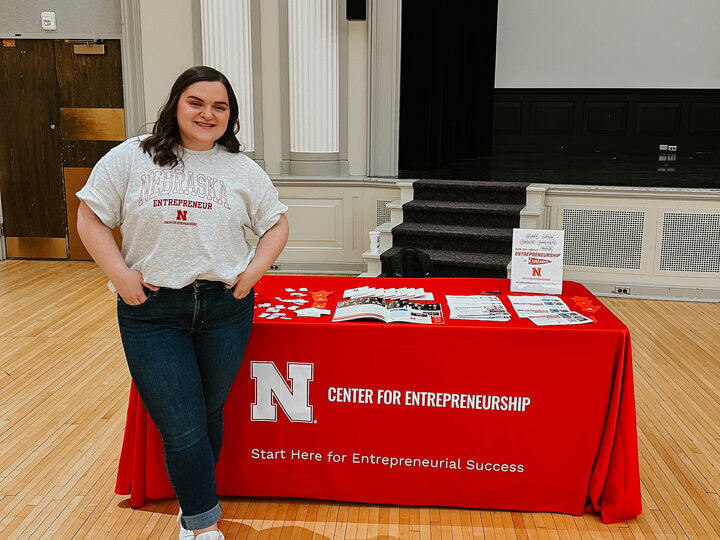 Mallory smiles as she stands in front of a Center for Entrepreneurship table in the City Campus Union.