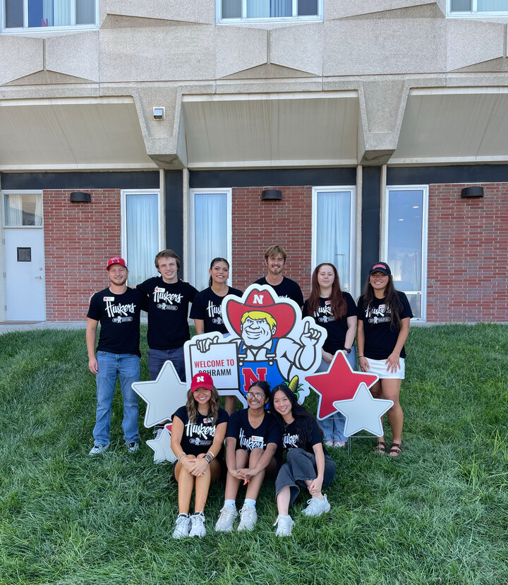 Group of people posing with a cutout Herbie mascot and decorative stars on grass.
