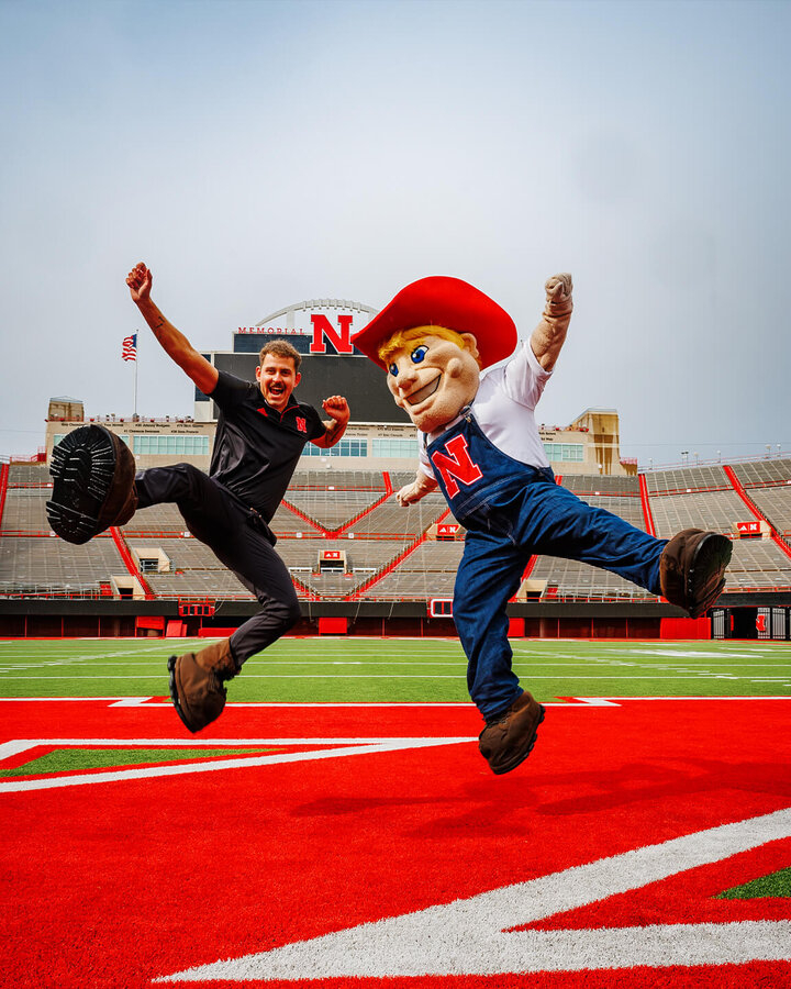 Connor, wearing Herbie Husker's shoes, and Herbie jump in the air with their arms outstretched