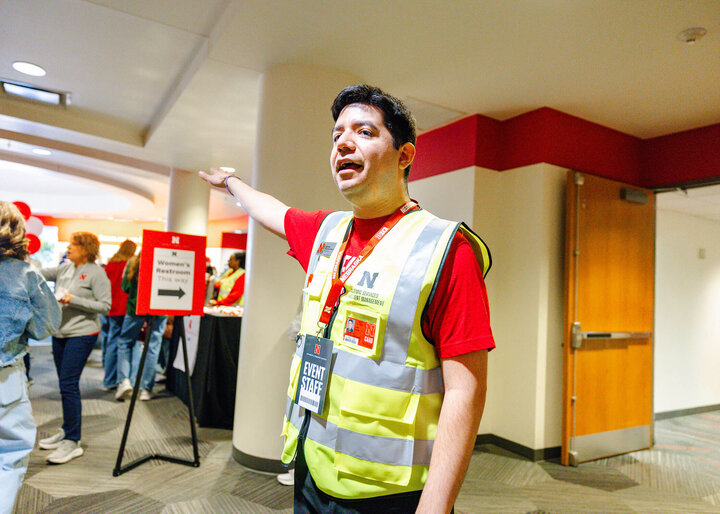 Lupe Perez wearing a safety vest points towards a crowded area in the Nebraska Union during the 2026 Admitted Students Day..